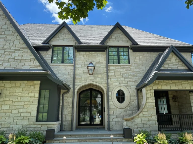 Luxury stone home in Naperville, IL with a new dark slate-look hip roof and copper gutters above a columned entry