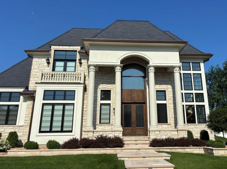 Luxury stone home in Naperville, IL with a new dark slate-look hip roof and copper gutters above a columned entry